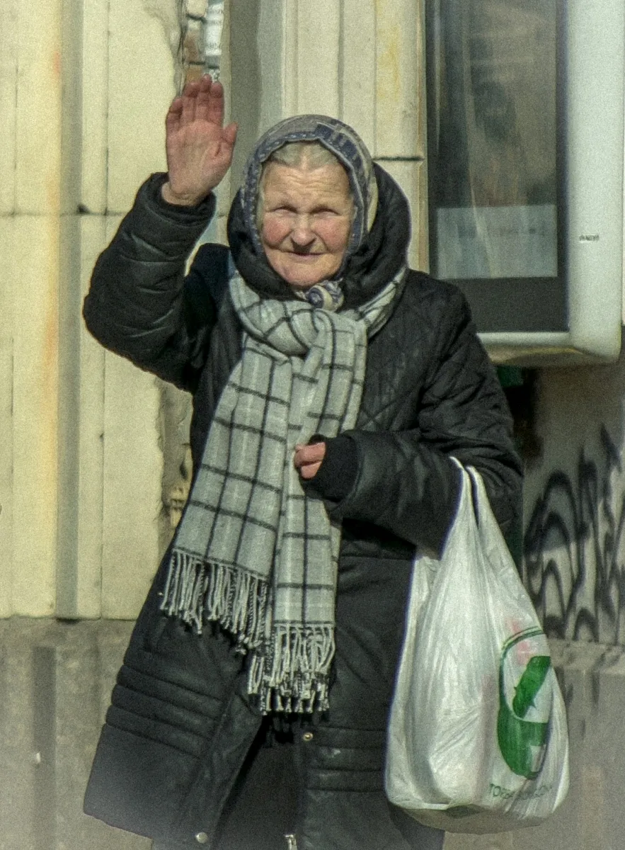 Older woman waving while carrying a white plastic bag